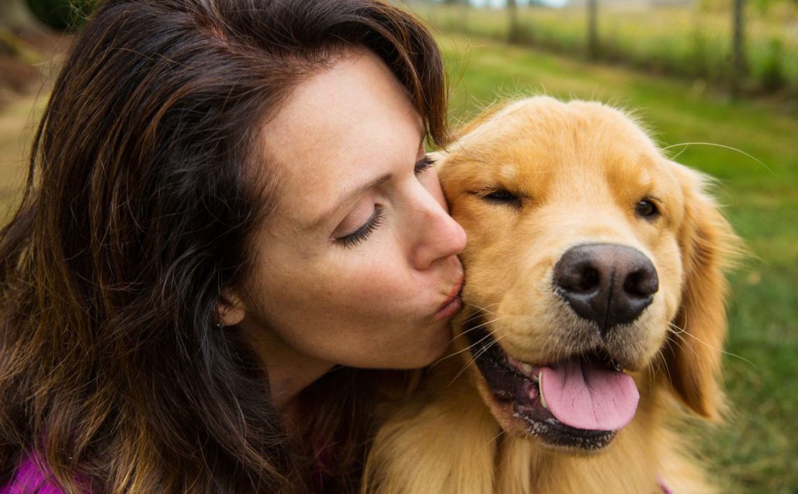 O femeie zâmbitoare sărutând pe obraz un câine Golden Retriever fericit, simbolizând prietenia ideală pentru un începător.