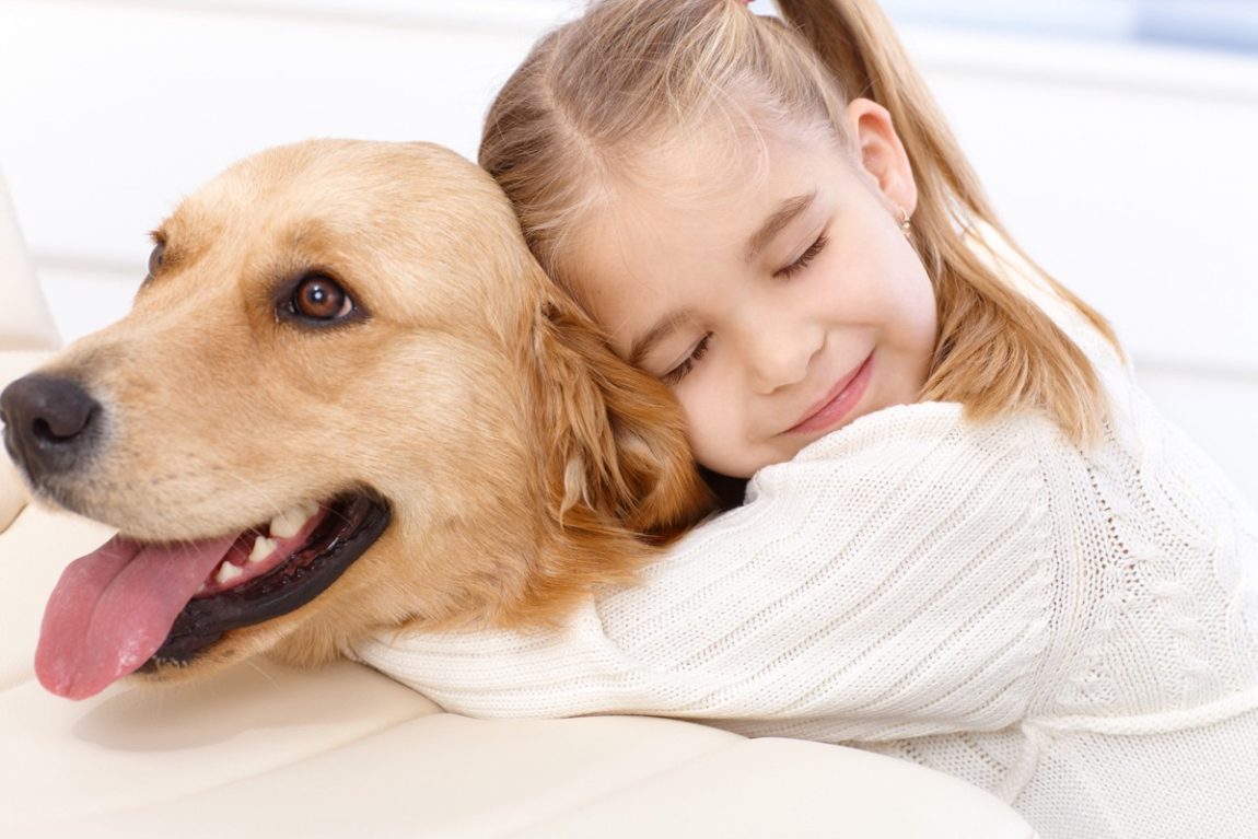O fetiță fericită cu ochii închiși îmbrățișează cu drag un câine Golden Retriever blând
